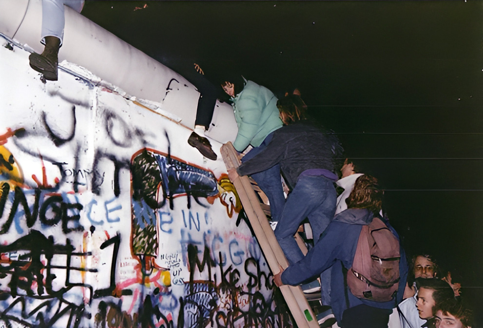 Der Fall der Berliner Mauer 1989: Mehrere Menschen klettern bei Nacht mit einer Leiter über die Mauer.